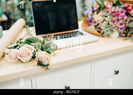 Bureau du fleuriste. Ordinateur portable sur la table, roses, eucalyptus, papier, fleurs. Banque D'Images