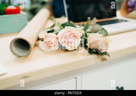 Bureau du fleuriste. Ordinateur portable sur la table, roses, eucalyptus, papier, fleurs. Banque D'Images