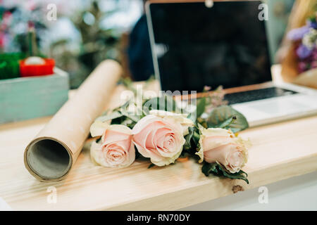 Bureau du fleuriste. Ordinateur portable sur la table, roses, eucalyptus, papier, fleurs. Banque D'Images