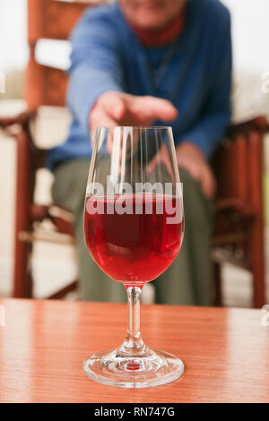 A senior woman sitting down atteindre pour prendre un verre de vin rouge sur une table à l'avant. UK Banque D'Images