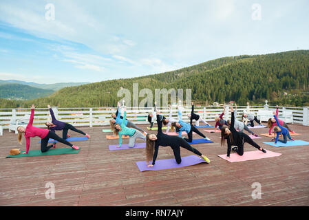 Groupe de femmes sportives faire du yoga ensemble en dehors de l'air frais. Les gens qui se posent à l'angle de côté a porté sur un tapis de yoga, de faire les exercices, la pratique de l'équilibre. Banque D'Images