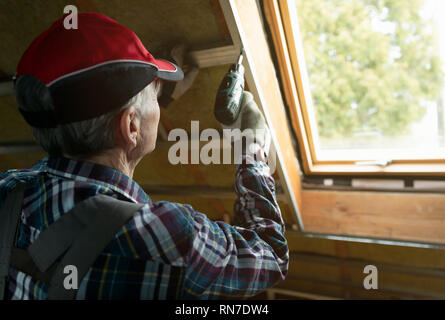 Isolation thermique des combles et la rénovation. Man fixing métal au moyen d'un tournevis électrique au plafond recouvert avec de la laine de roche Banque D'Images