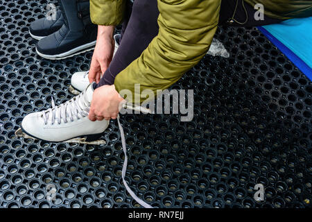 Une jeune femme lacets attachés sur patins blanc avant de monter une patinoire 2019 Banque D'Images