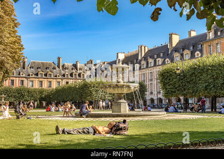 Personnes assises et bains de soleil sur les pelouses près de la fontaine de la place des Vosges , dans le quartier à la mode du Marais de Paris, France Banque D'Images