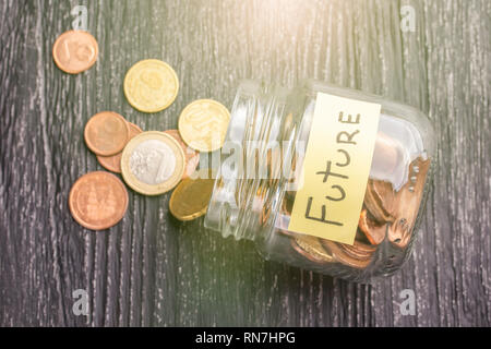 Pot en verre incliné ouvert avec des pièces en euros à l'inscription l'avenir sur une table en bois noir. Le concept de l'épargne pour le prospect Banque D'Images