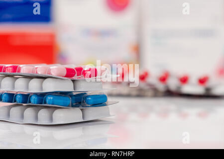 Medical pills en blanc, bleu et autres couleurs sur fond miroir blanc. Comprimés en emballage en plastique. Notion de santé et médecine. Banque D'Images