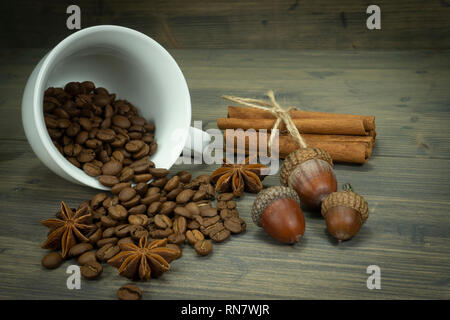 Les grains de café torréfié de renverser une tasse, de glands et de cannelle à la badiane spice sur une table en bois rustique dans une vue en gros plan Banque D'Images