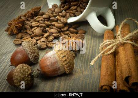 Les grains de café torréfié de renverser une tasse, de glands et de cannelle à la badiane spice sur une table en bois rustique dans une vue en gros plan Banque D'Images