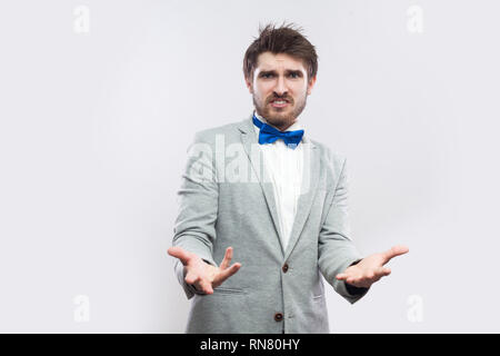 Que voulez-vous ? Portrait d'homme barbu beau en colère en costume gris, noeud papillon bleu, debout les bras levés, à la caméra et à demander à l'intérieur. Banque D'Images