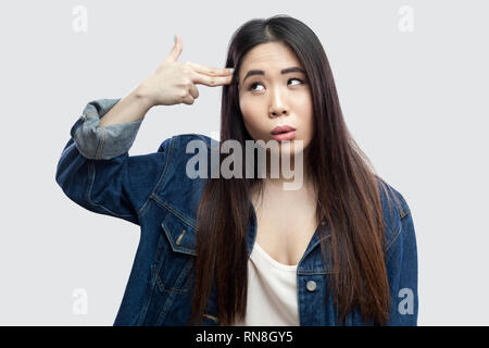 Portrait de seul déprimé belle brune asian young woman in casual veste en jean bleu avec un miroir debout avec fusil pistolet sur la tête. Piscine stu Banque D'Images