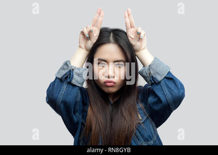 Portrait d'une belle brunette asian young woman in casual veste en jean bleu avec un miroir avec des cornes et permanent à la caméra à l'intérieur. stu Banque D'Images