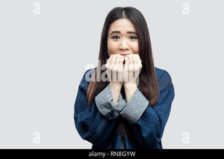 Portrait d'un choc nerveux belle brune asian young woman in casual veste en jean bleu avec le maquillage ongles son mordant permanent et à la recherche en est venu Banque D'Images