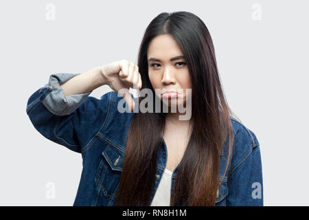 Portrait d'insatisfaits belle brune jeune femme asiatique en veste bleue avec un miroir et permanent à la recherche à l'appareil photo avec vers le bas et l'aversion. Banque D'Images