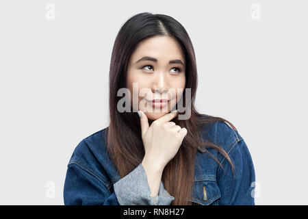 Portrait de smiley rêveur belle brune asian young woman in casual veste en jean bleu avec le maquillage L'article touchant son menton et méditant. indoo Banque D'Images