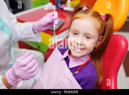 L'enfant est un peu red-haired girl smiling assis dans un fauteuil dentaire. Banque D'Images