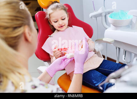 Dentiste montre la petite fille comment nettoyer les dents avec une brosse à dents sur une mâchoire artificielle dummy Banque D'Images