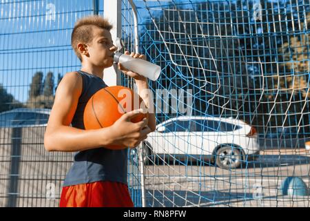 Adolescents jouant au basket-ball de rue avec ballon de basket-ball de la ville de plein air sur l'eau potable. Banque D'Images