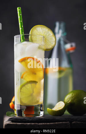 Boisson tonique avec citron et de lime dans un verre transparent avec une bouteille ouverte sur une table en bois Banque D'Images