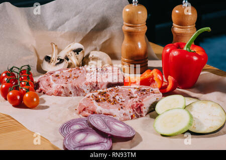 Les steaks juteux avec les assaisonnements et les légumes frais mûrs sur papier Banque D'Images