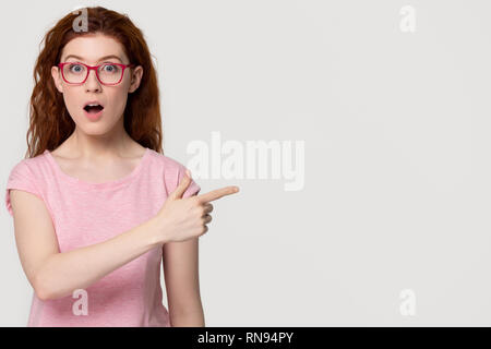 Surpris redhead girl student en lunettes roses au pointage copyspace Banque D'Images