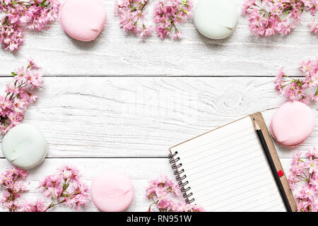Maquette de papier vierge dans le châssis de l'ordinateur portable fait de branches de printemps en fleurs rose cerise et macarons avec copie espace. vue d'en haut. télévision lay Banque D'Images