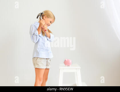 Petite fille avec un marteau par la tirelire cochon rose sur fond blanc Banque D'Images