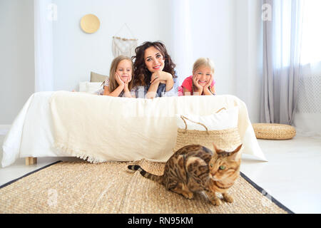 Heureux d'une mère et de deux de ses filles smiling câlins au lit. Famille heureuse à la maison avec le chat d'intérieur Banque D'Images