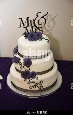 Portrait de monsieur et madame gâteau de mariage sur mariage. A gâteau glaçage blanc, ruban violet et le sucre fleurs violettes le décorer. Banque D'Images