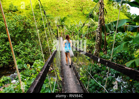 Jeune femme marche sur pont suspendu au-dessus de Wainibau stream, Lavena promenade côtière, l'île de Taveuni (Fidji). Taveuni est la troisième plus grande île des Fidji. Banque D'Images