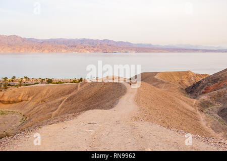 Courbe de sable autour de la voie des montagnes du désert jusqu'à la mer Rouge bay shore et les plages d'Eilat, Israël avec la Jordanie l'autre sur l'arrière-plan Banque D'Images