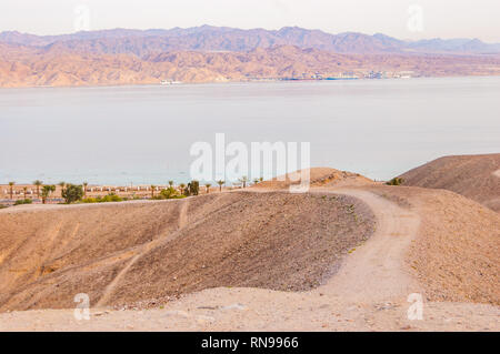 Courbe de sable autour de la voie des montagnes du désert jusqu'à la mer Rouge bay shore et les plages d'Eilat, Israël avec la Jordanie l'autre sur l'arrière-plan Banque D'Images