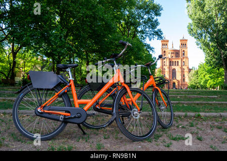 Deux vélos orange garé vers Saint Thomas l'église protestante Saint-thomas () à Berlin, Allemagne. Vélo urbain partager concept pour week-end et gateaways Banque D'Images