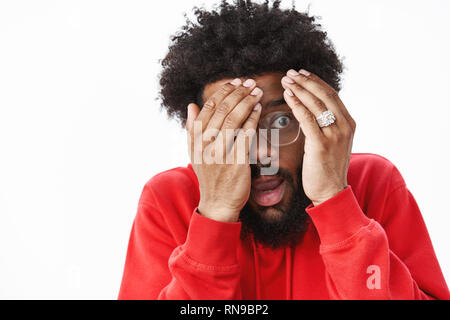 De façon intéressante, mais spooky. Portrait d'intrigué et effrayé les jeunes afro avec ventilateur horreur hairstyle et beard, bouche ouverte, mains et visage fermer Banque D'Images