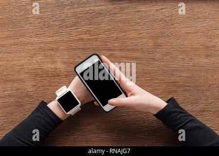 Portrait de fille avec smartwatch avec holding Smartphone avec écran blanc sur fond de bois Banque D'Images