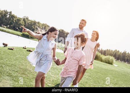 Le collage. Famille de quatre personnes marchant sur un terrain herbeux près du lac enfants marchant devant se tenant la main tandis que les parents derrière hugging Banque D'Images