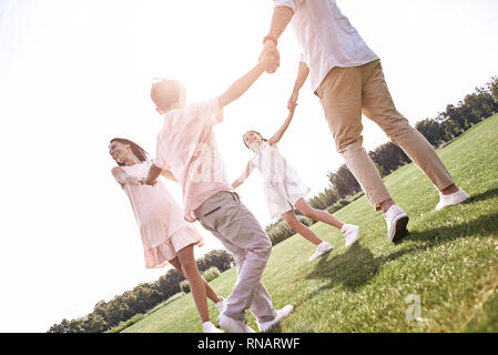 Le collage. Famille de quatre personnes se tenant la main la danse de cercle sur un terrain herbeux fond voir le sourire heureux Banque D'Images