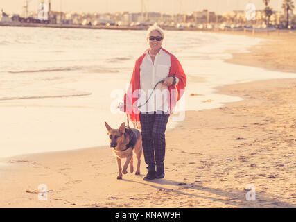 Belle femme plus âgée à la retraite et pet dog allemand shepard marcher le long de la côte sur l'océan mer plage en compagnie d'animaux Prestations activ maintien Banque D'Images