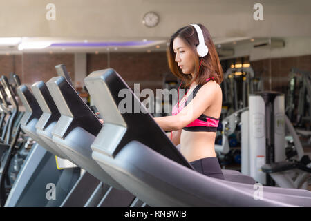 Jeune fille portant un costume rose blanc exercice est la marche sur le tapis roulant dans le centre de remise en forme ou un gymnase. Banque D'Images