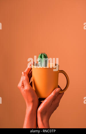 Vue partielle de woman holding Coffee cup avec corail cactus vert sur fond de corail, la couleur de 2019 concept Banque D'Images