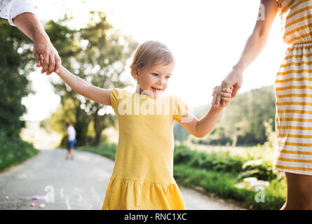 Un portrait de famille avec petite fille jouant à la marelle sur une route en été. Banque D'Images