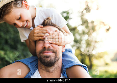 Jeune père dans la nature aurait petit fils un piggyback ride, garçon couvrant les yeux de l'homme. Banque D'Images