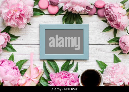 Carte photo vierge dans cadre fait de fleurs de pivoine rose, macarons et café tasse blanche sur fond de bois. Télévision. vue d'en haut.. la maquette ou mariage f Banque D'Images