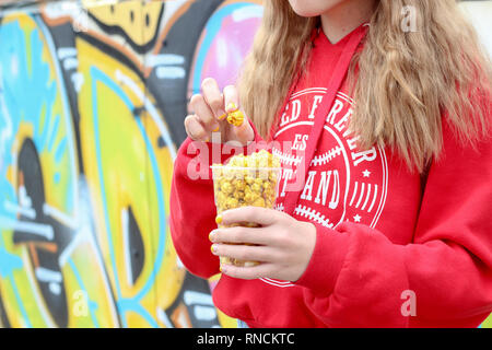 Jeune fille tenant un pot de pop-corn d'or contre le mur de graffiti dans le parc Banque D'Images