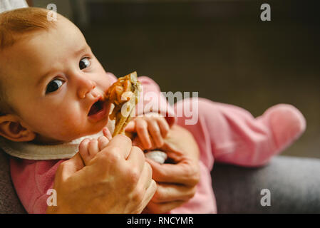 4 mois du grignotage une cuisse de poulet, sa première dégustation des aliments à l'aide de la méthode de sevrage led Bébé BLW. Banque D'Images