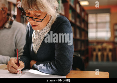 Senior woman sitting in classroom et prendre des notes. Apprentissage chez les aînés assis dans une salle de classe universitaire. Banque D'Images