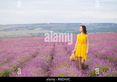 Belle jeune femme en robe jaune avec un chapeau dans les mains se détendre et s'amuser sur champ de lavande fleurs de mauve. Banque D'Images