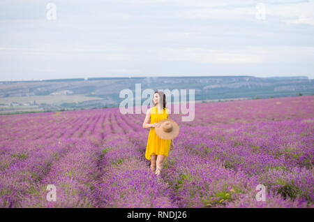 Belle jeune femme en robe jaune avec un chapeau dans les mains se détendre et s'amuser sur champ de lavande fleurs de mauve. Banque D'Images