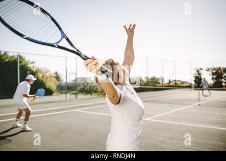 Vue arrière d'une femme le ballon tout en jouant un match de tennis en double mixte. Les hommes et les femmes à jouer au tennis à l'extérieur sur une journée ensoleillée. Banque D'Images