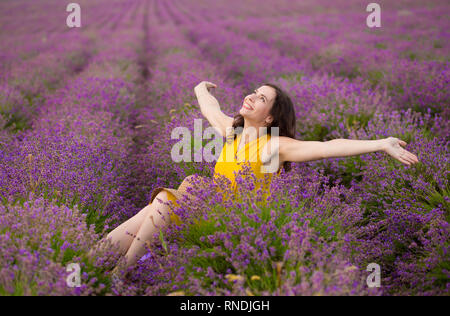 Belle jeune femme en robe jaune avec un chapeau dans les mains se détendre et s'amuser sur champ de lavande fleurs de mauve. Banque D'Images