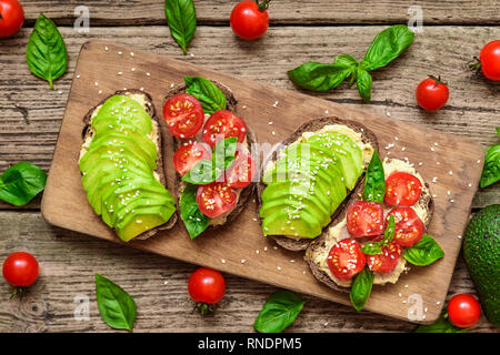 Petit-déjeuner sandwiches avec de l'avocat, les tomates, le basilic, l'hoummos et graines de sésame sur une planche à découper rustique. Collation santé. Vue de dessus Banque D'Images